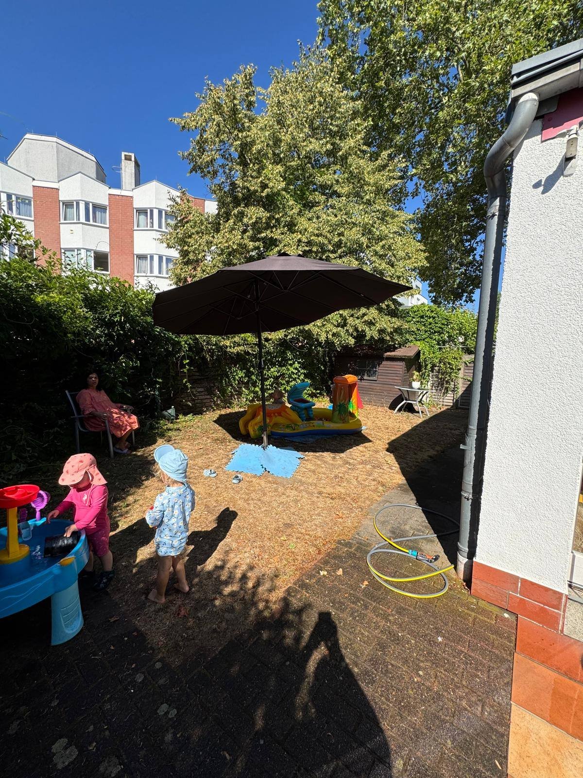 Blick in den Garten mit Sonnenschirm, Wasserspieltisch und Wiese