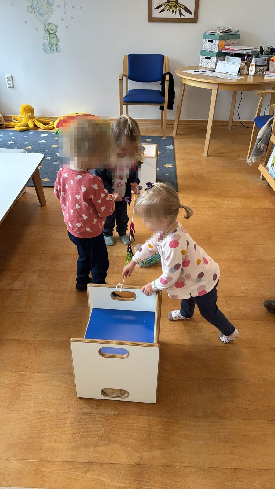Drei Kinder spielen gemeinsam mit Wäscheklammern und einer Holzkiste