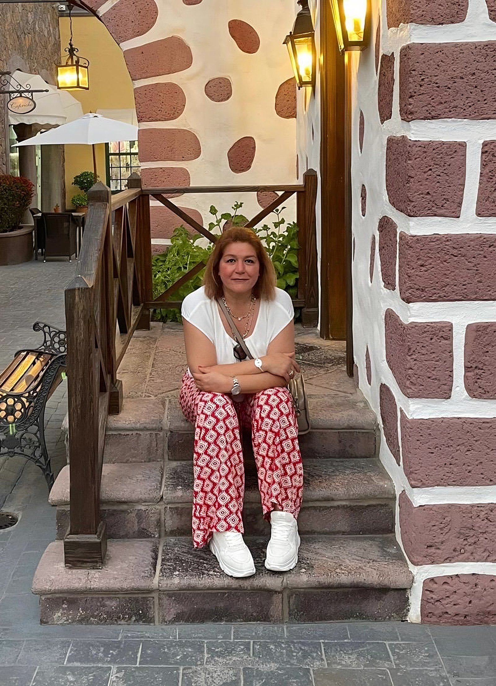 Parissa Geraminejad sitzt lächelnd auf einer Steintreppe vor einem hellen Torbogen