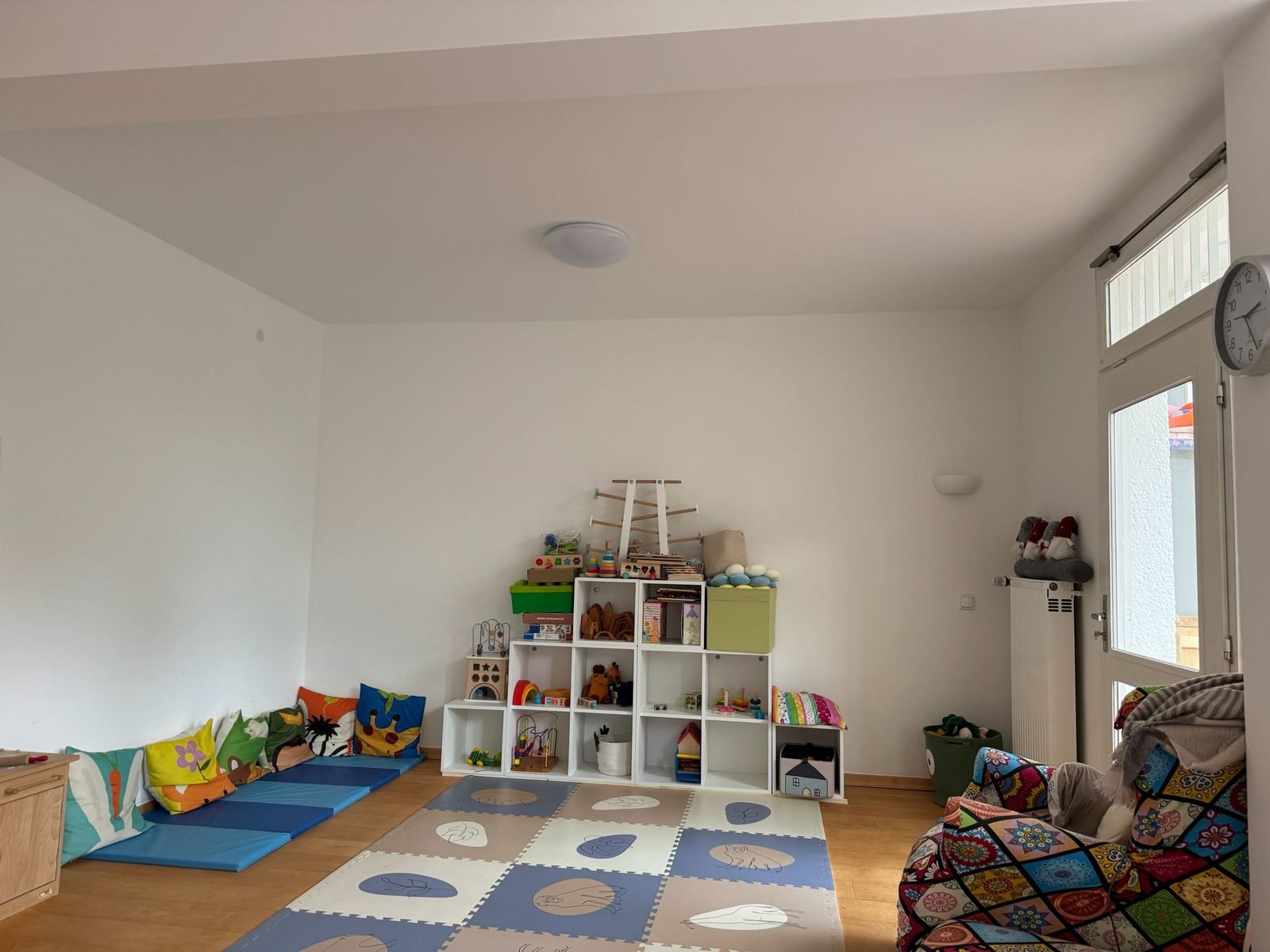 Helles Spielzimmer mit Spielmatten, Kissen und Regalen voller Spielsachen